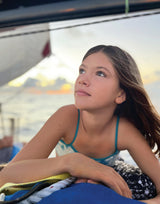 Girl on a boat wearing a swimsuit, looking thoughtful at sunset over water.